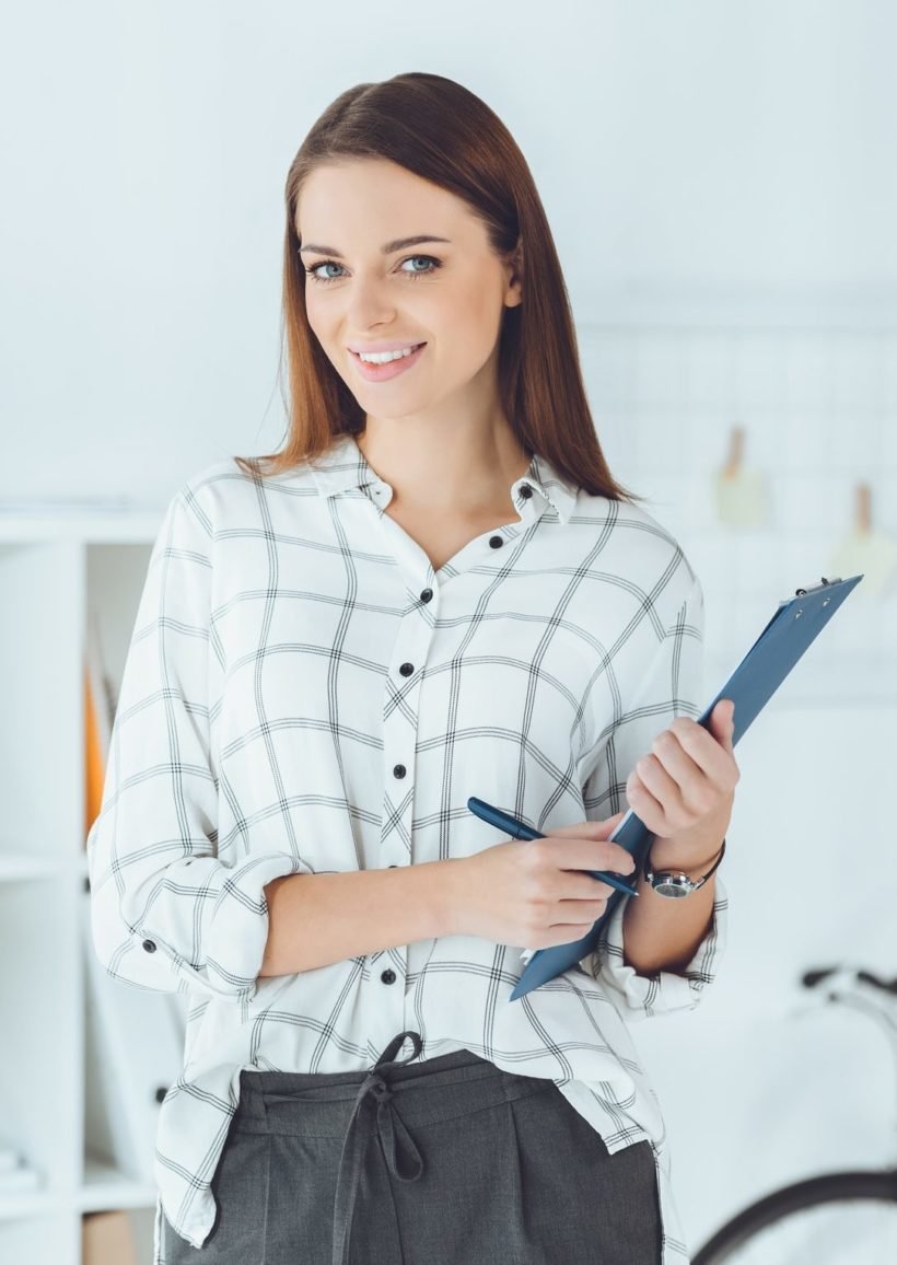 smiling businesswoman with clipboard and pencil looking at camera e1645410716773